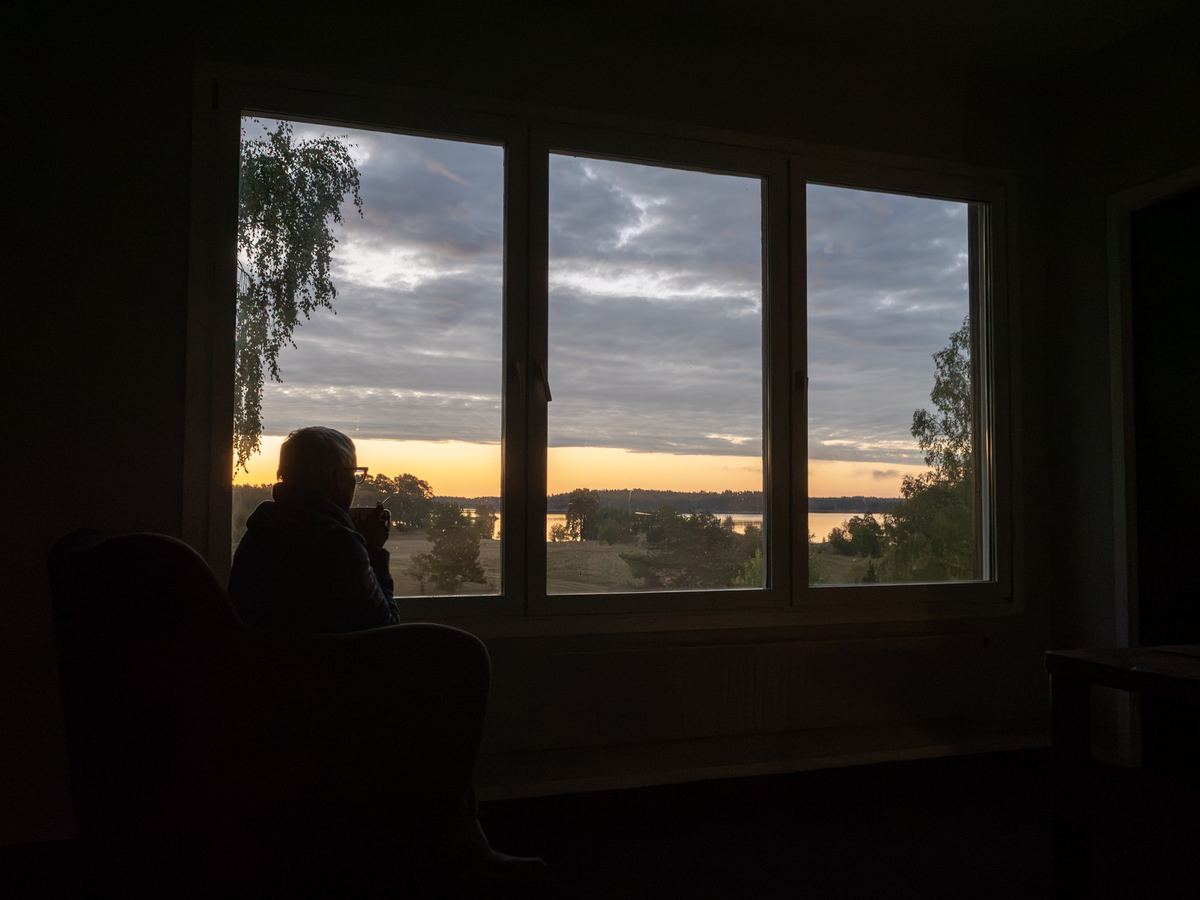 En person i siluett vid ett stort fönster med utsikt över sjön i gryningen.
