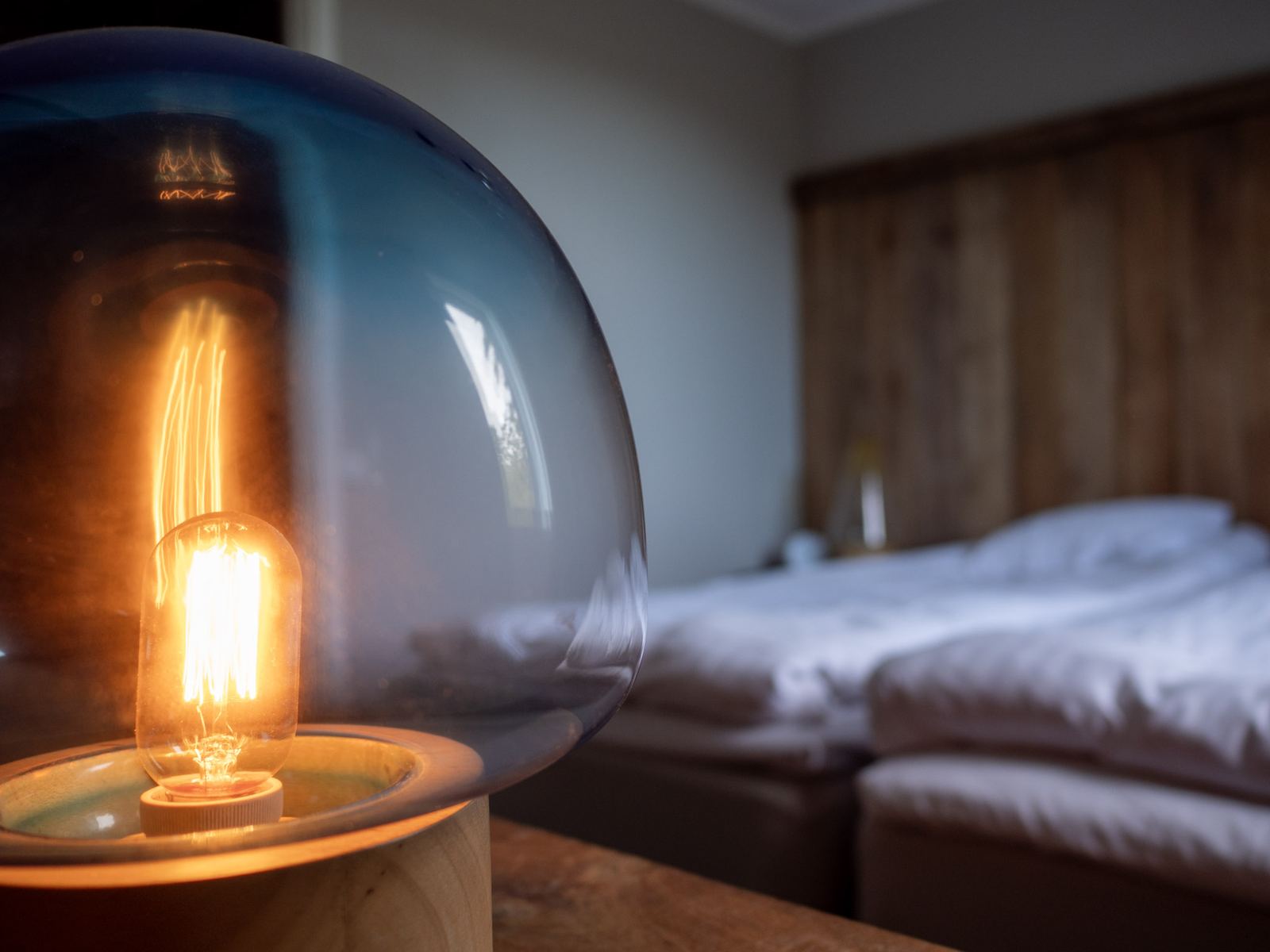 En tänd lampa bredvid en bäddad säng.