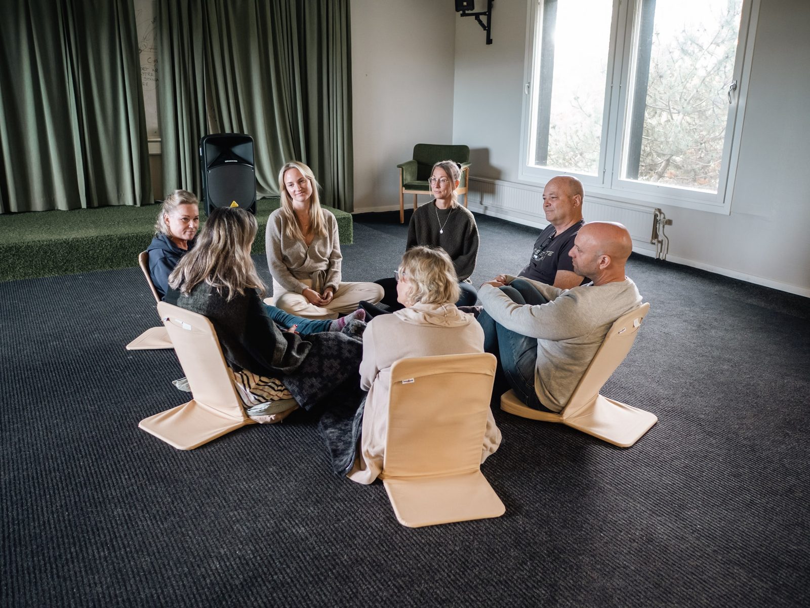 Participants sitting in a circle on floor chairs in a bright room.