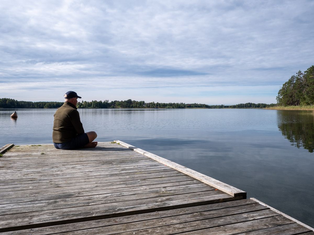 En person sitter på en brygga och ser ut över sjön.