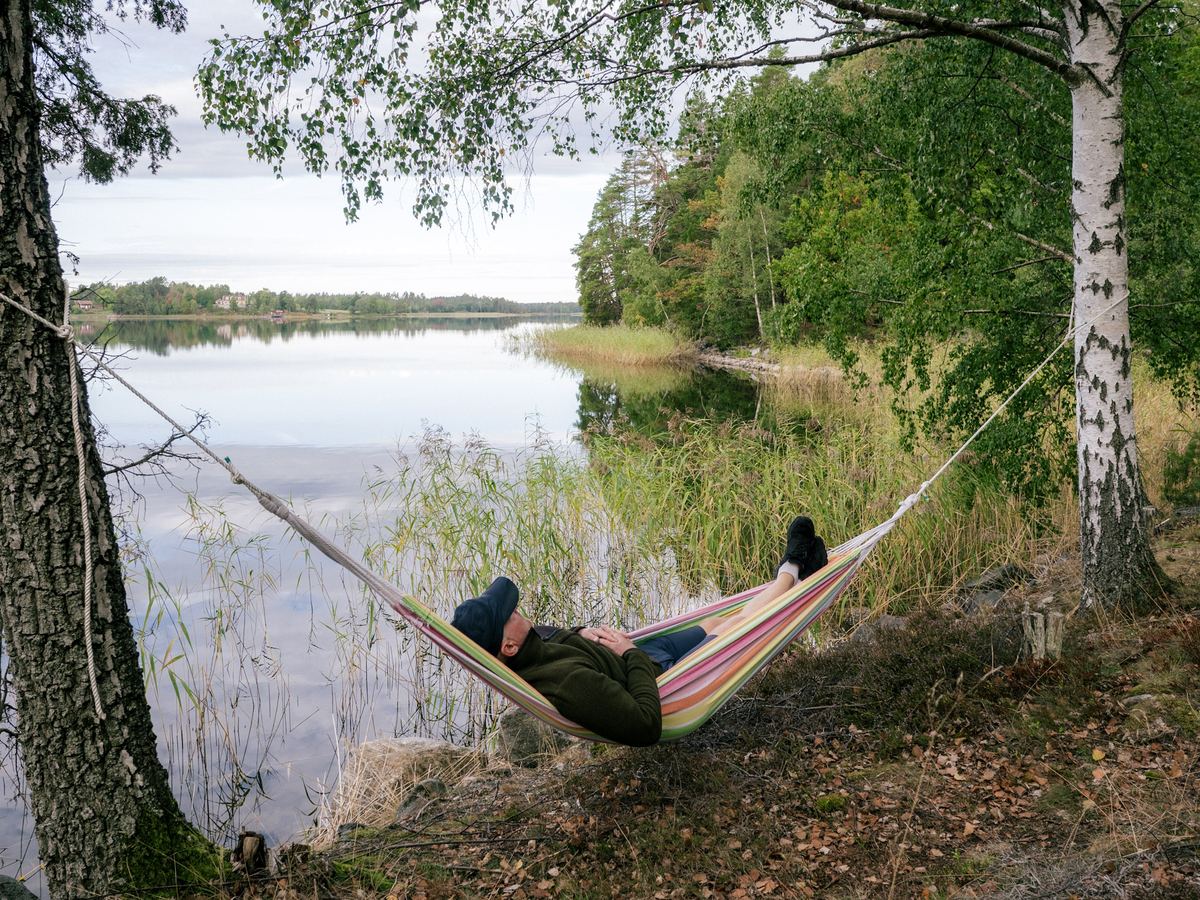 En person vilar i en hängmatta mellan träden vid sjön.