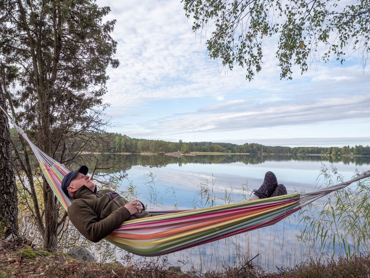 En person vilar i en randig hängmatta vid sjön.
